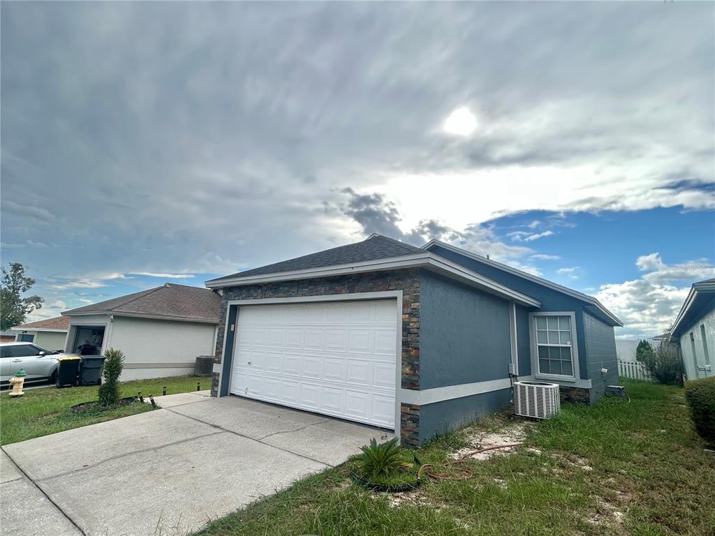 A blue house with a stone-accented garage and a concrete driveway under a cloudy sky — 622 CRYSTALS BOULEVARD, WINTER HAVEN, FL