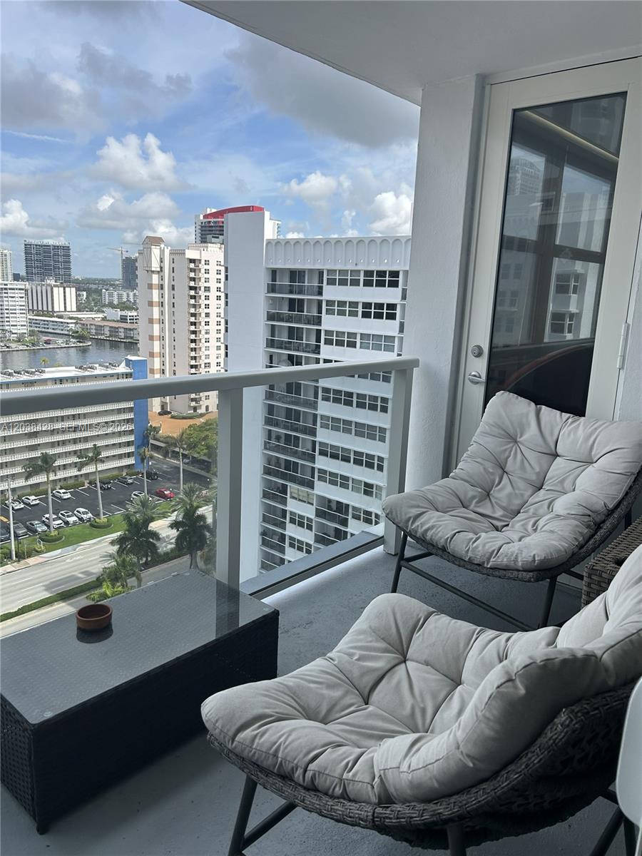 A balcony with two cushioned chairs and a small table overlooks a city skyline — 1904 S Ocean Dr # 1807, Hallandale Beach FL 33009, HALLANDALE BEACH, FL