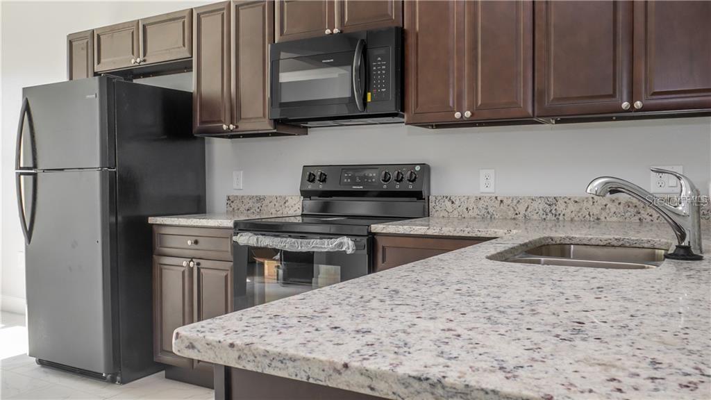 A kitchen features dark wood cabinets, granite countertops, and black appliances — 401 ALBATROSS COURT UNIT B, KISSIMMEE, FL
