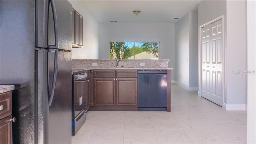 A kitchen features dark wood cabinets, granite countertops, black appliances, and light-colored tile flooring — 401 ALBATROSS COURT UNIT B, KISSIMMEE, FL