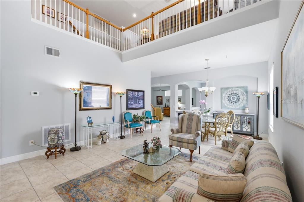 A high-ceilinged living room features tile flooring, a glass coffee table, and a lofted balcony — 5011 CORTO DRIVE, ORLANDO, FL
