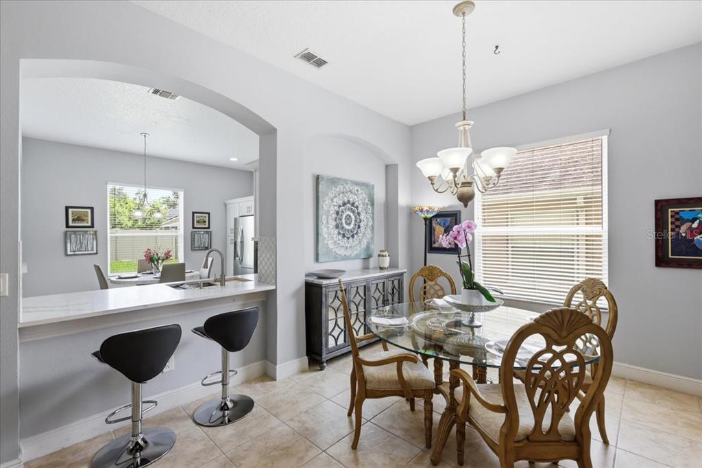 A dining area with a glass table, ornate chairs, and a breakfast bar with stools — 5011 CORTO DRIVE, ORLANDO, FL