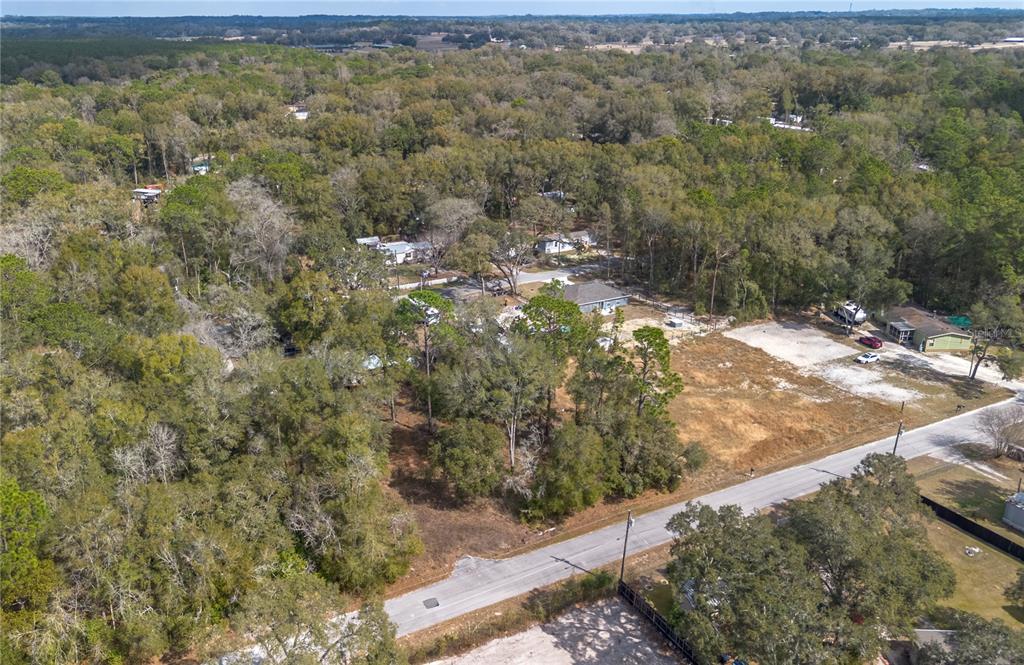 An aerial view shows a wooded lot next to a cleared area and a road — NW 13TH STREET, OCALA, FL