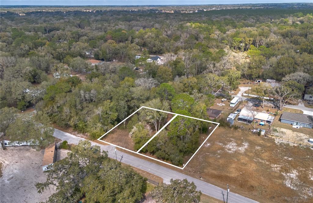An aerial view shows two adjacent, undeveloped wooded lots along a paved road — NW 13TH STREET, OCALA, FL