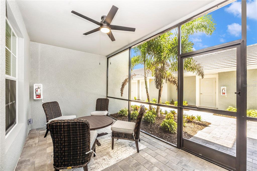 A screened-in patio features wicker furniture, a ceiling fan, and a view of palm trees — 17500 OPAL SAND DRIVE UNIT 101, VENICE, FL