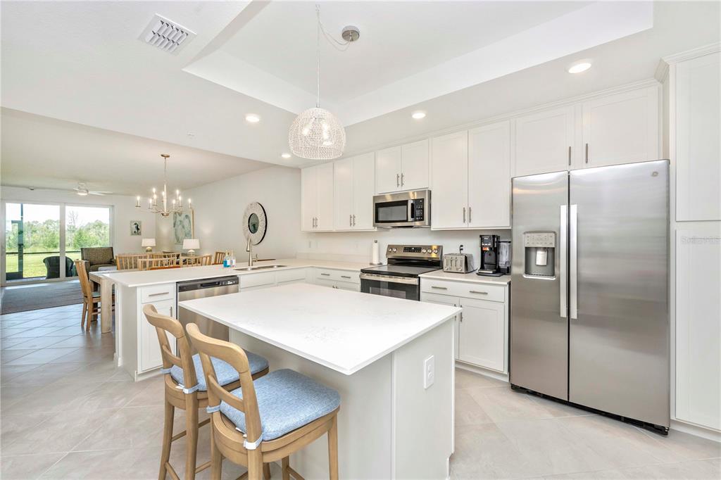 A modern kitchen features white cabinetry, stainless steel appliances, a central island, and tile flooring — 17500 OPAL SAND DRIVE UNIT 101, VENICE, FL