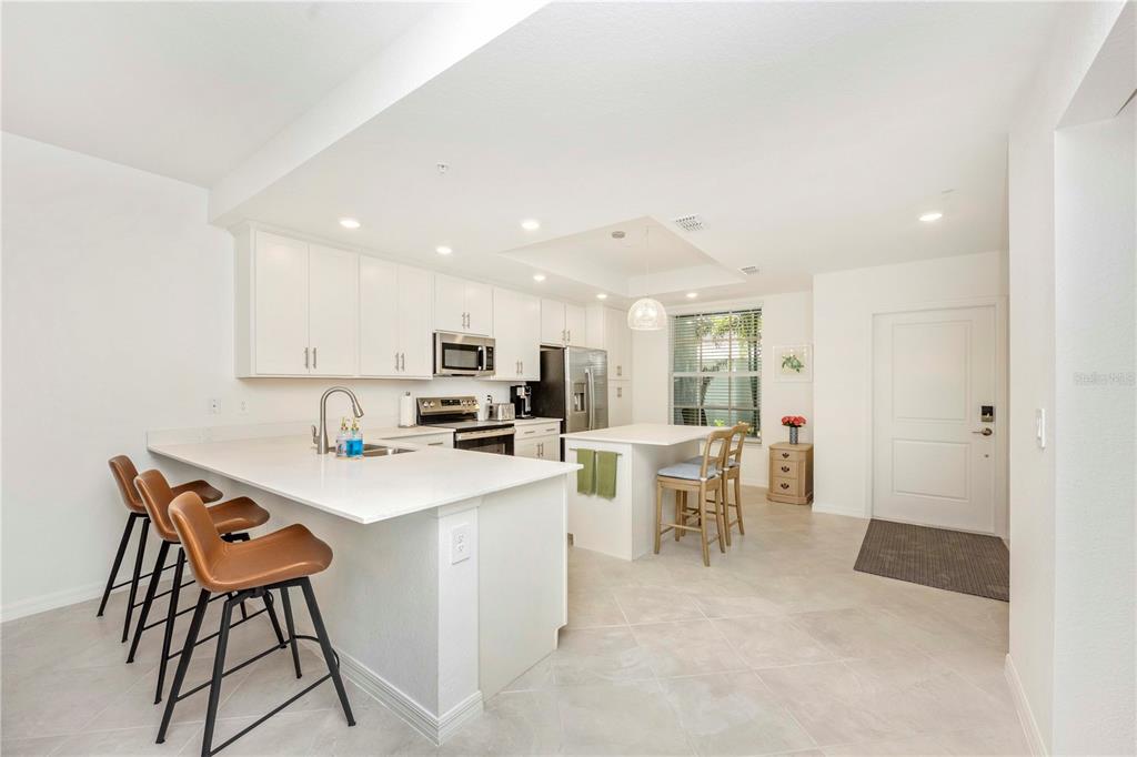 A modern kitchen features white cabinetry, a quartz island with bar seating, and tile flooring — 17500 OPAL SAND DRIVE UNIT 101, VENICE, FL