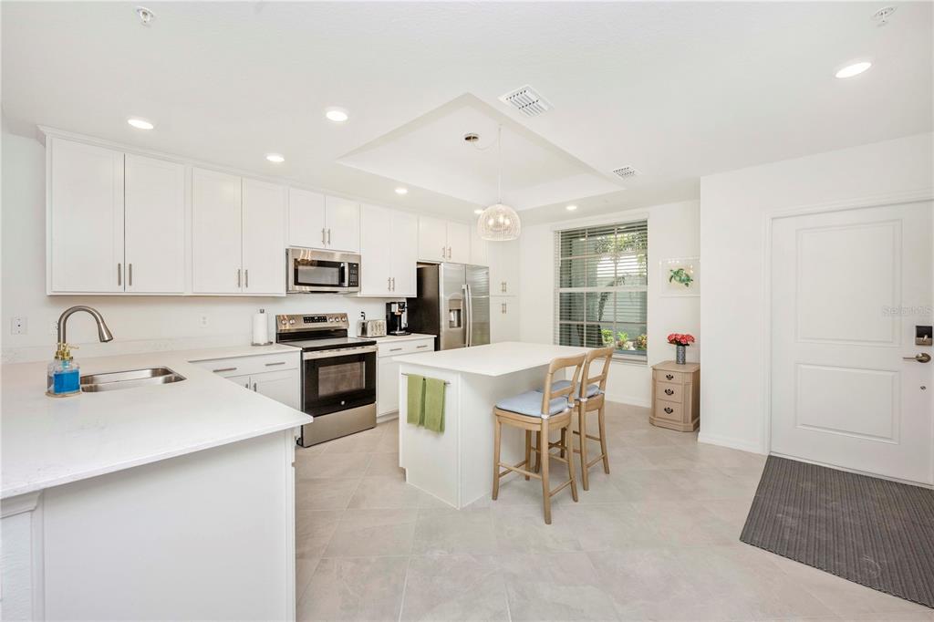 A modern kitchen features white cabinetry, a central island with bar seating, and stainless appliances — 17500 OPAL SAND DRIVE UNIT 101, VENICE, FL