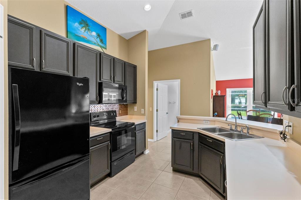 A kitchen with dark cabinets, black appliances, light countertops, and tile flooring — 949 ROSINIA COURT, ORLANDO, FL