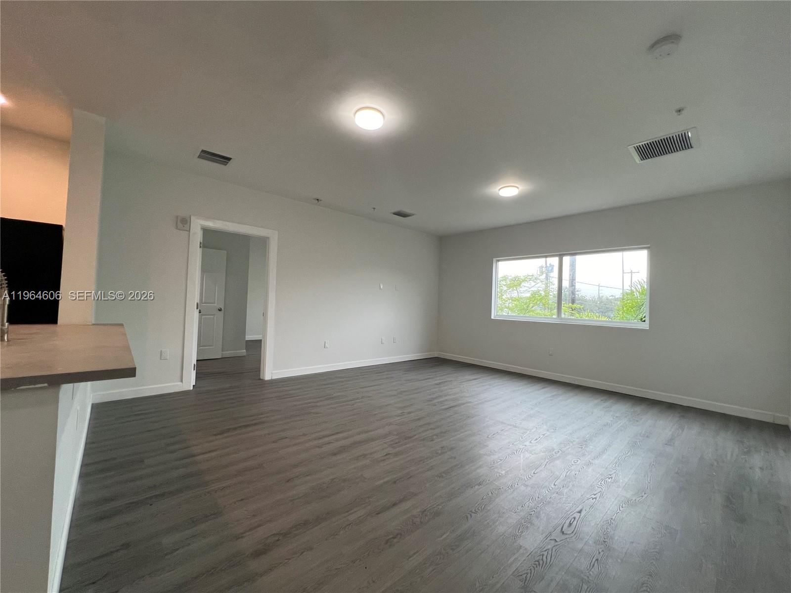 An unfurnished living area features light gray walls, dark wood-look flooring, and a large window — 2311 NW 22nd Ave # 405, Miami FL 33142, MIAMI, FL