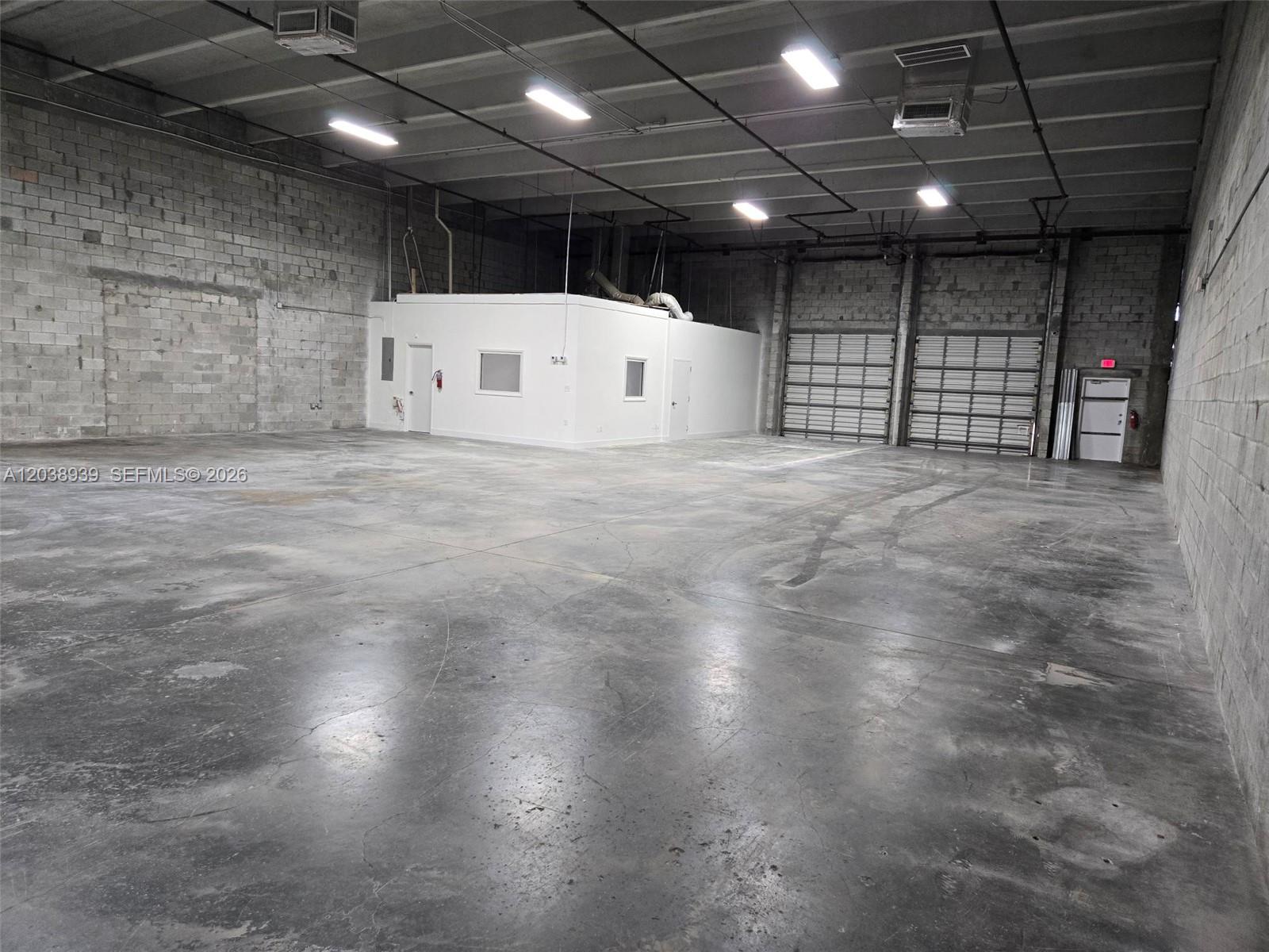This industrial warehouse space features concrete block walls, a concrete floor, and two roll-up doors — HIALEAH, FL