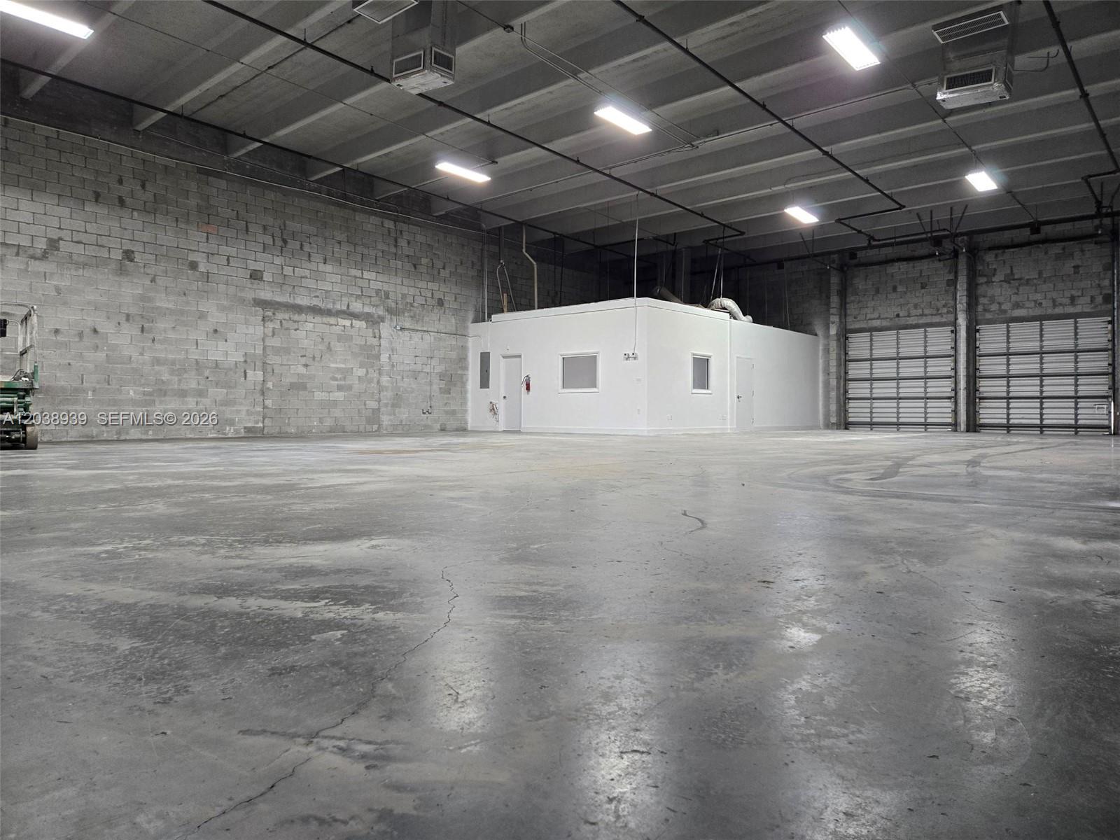A large industrial warehouse space features a concrete floor, block walls, and a central office — HIALEAH, FL