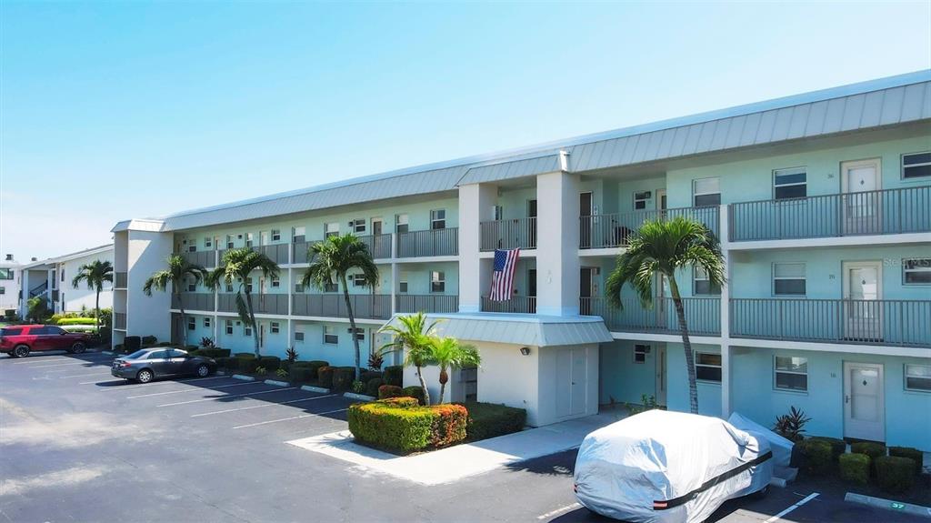An exterior view of a three-story apartment building with a parking lot and palm trees — 9200 MIDNIGHT PASS ROAD UNIT 24, SARASOTA, FL