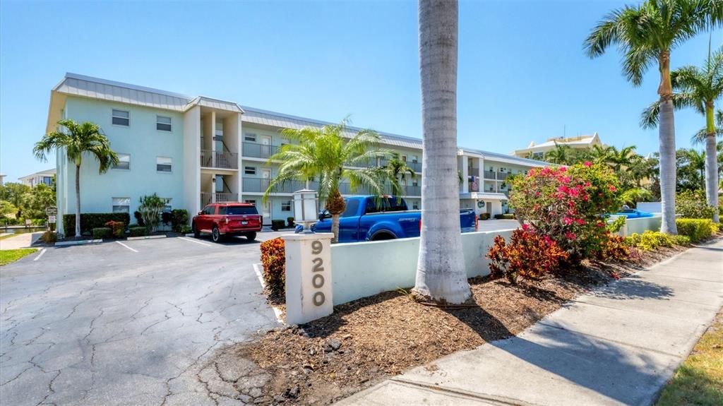 A three-story apartment building with a parking lot and palm trees in front — 9200 MIDNIGHT PASS ROAD UNIT 24, SARASOTA, FL