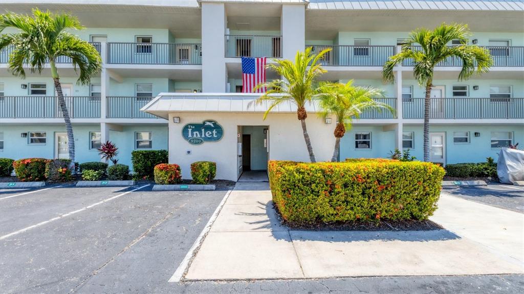 The exterior of a multi-story apartment building features a central entrance, palm trees, and landscaping — 9200 MIDNIGHT PASS ROAD UNIT 24, SARASOTA, FL