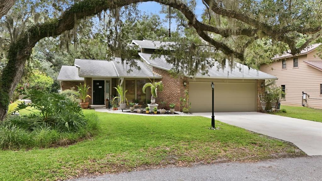 A single-story brick house with a two-car garage sits behind a large, moss-draped oak tree — 1063 GREYSTONE LANE, SARASOTA, FL