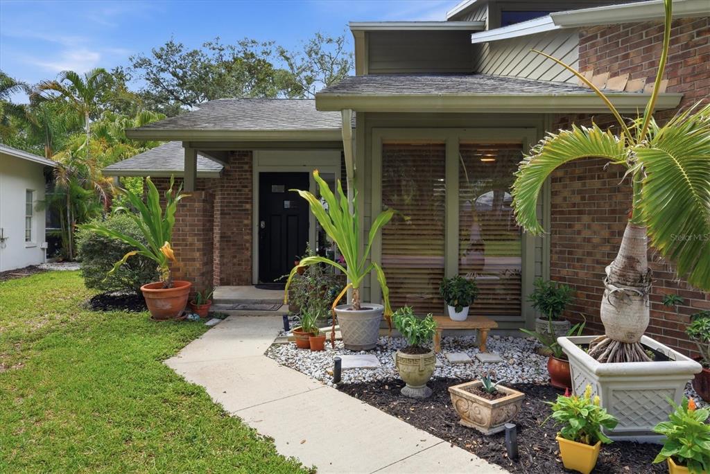 The exterior of a brick house features a front walkway, potted plants, and a black door — 1063 GREYSTONE LANE, SARASOTA, FL