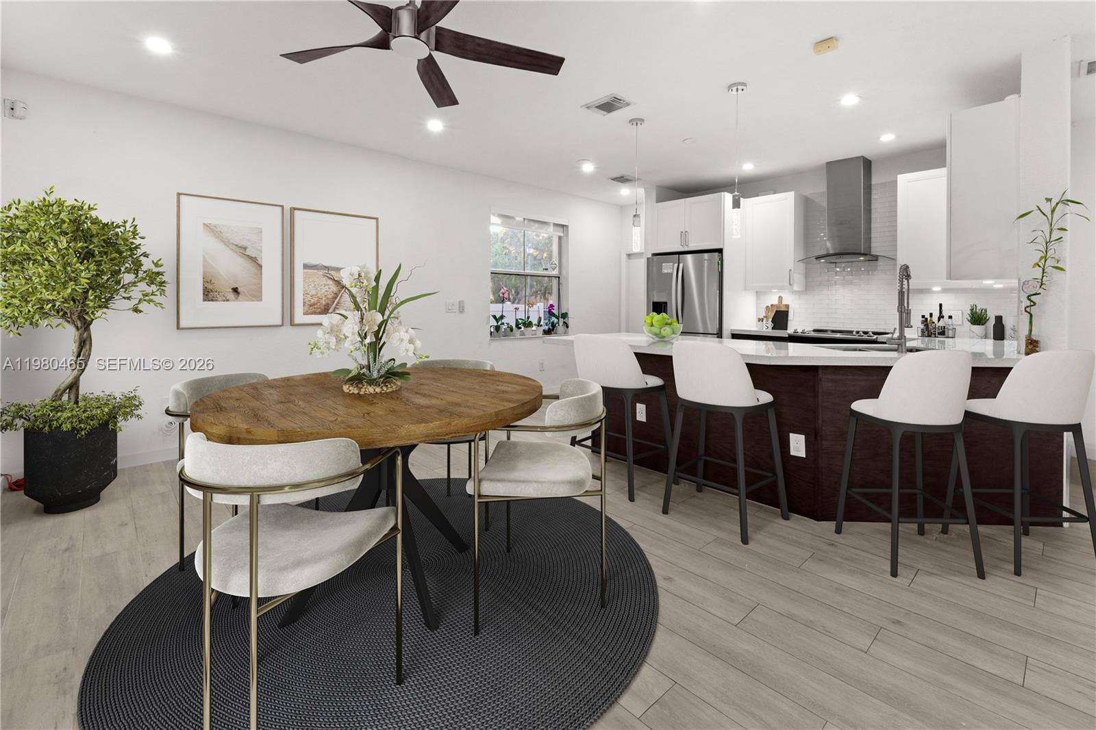 A dining area with a round wooden table sits adjacent to a modern kitchen island — 17130 SW 36th Ct, Miramar FL 33027, MIRAMAR, FL
