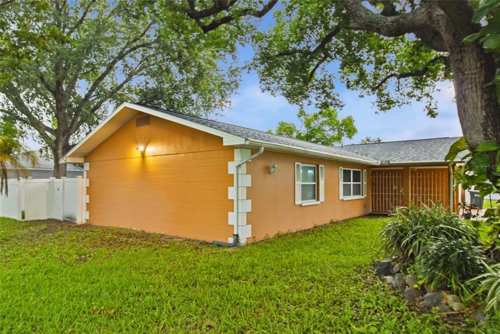 A single-story house with orange stucco walls, white corner accents, and a gray shingled roof — 11351 130TH AVENUE, LARGO, FL