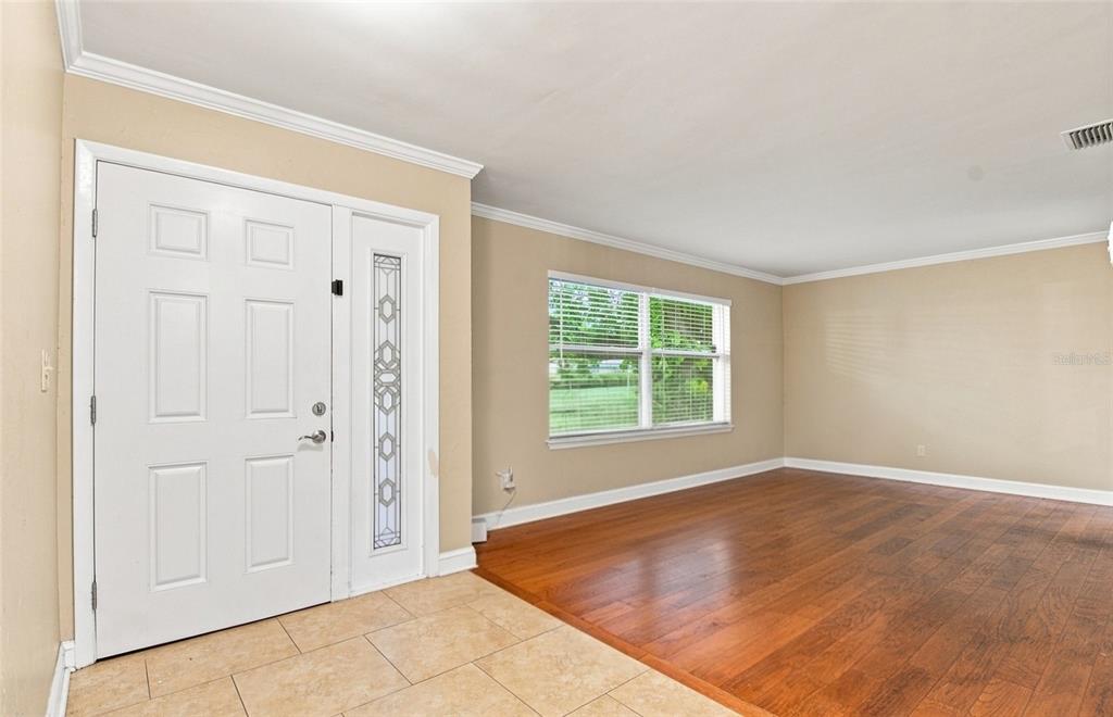An entryway with tile flooring transitions into a living room featuring hardwood floors and windows — 11351 130TH AVENUE, LARGO, FL