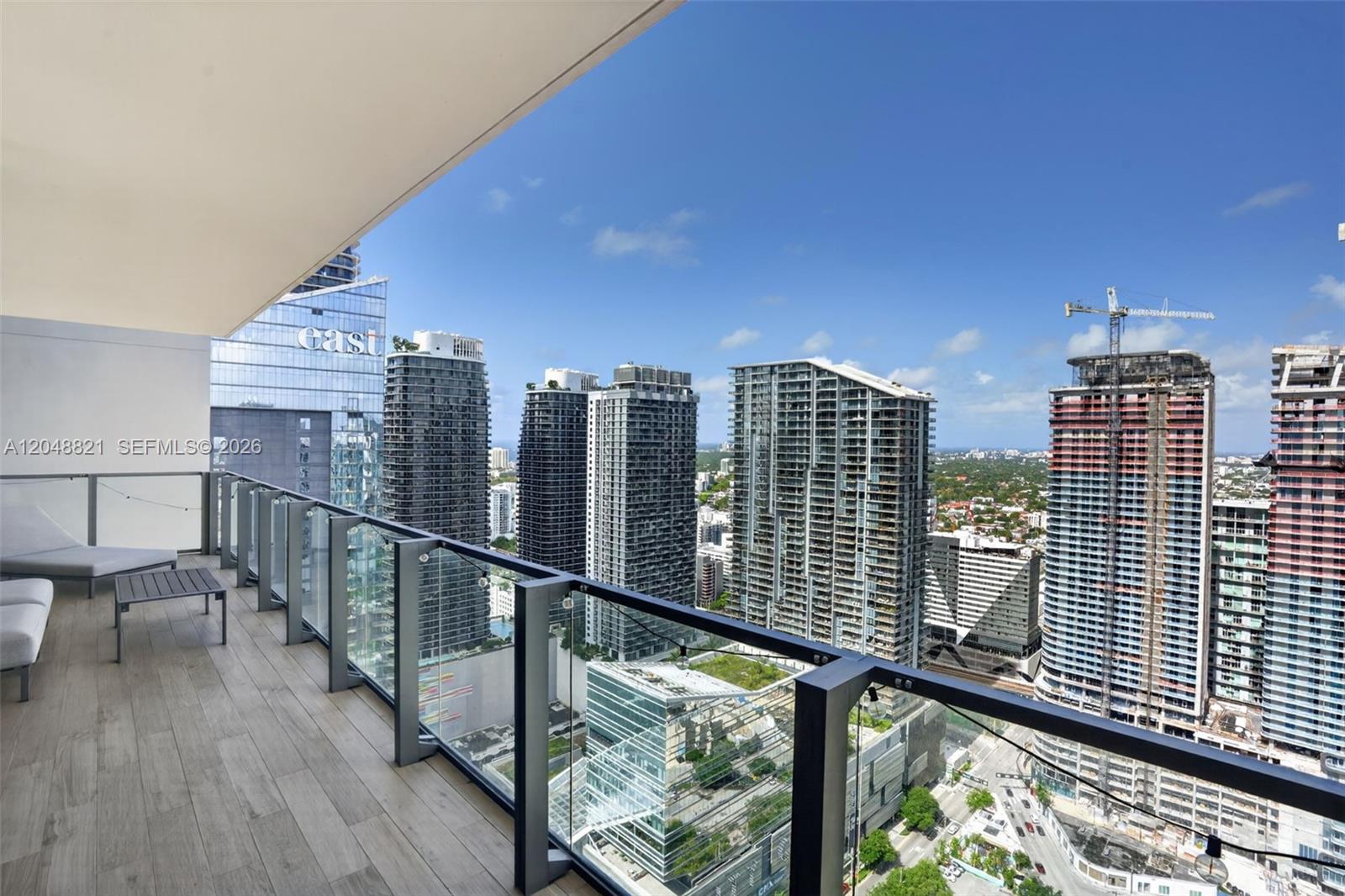 A balcony with wood-look tile flooring overlooks a dense urban skyline with several skyscrapers — 68 SE 6th St # 3710, Miami FL 33131, MIAMI, FL