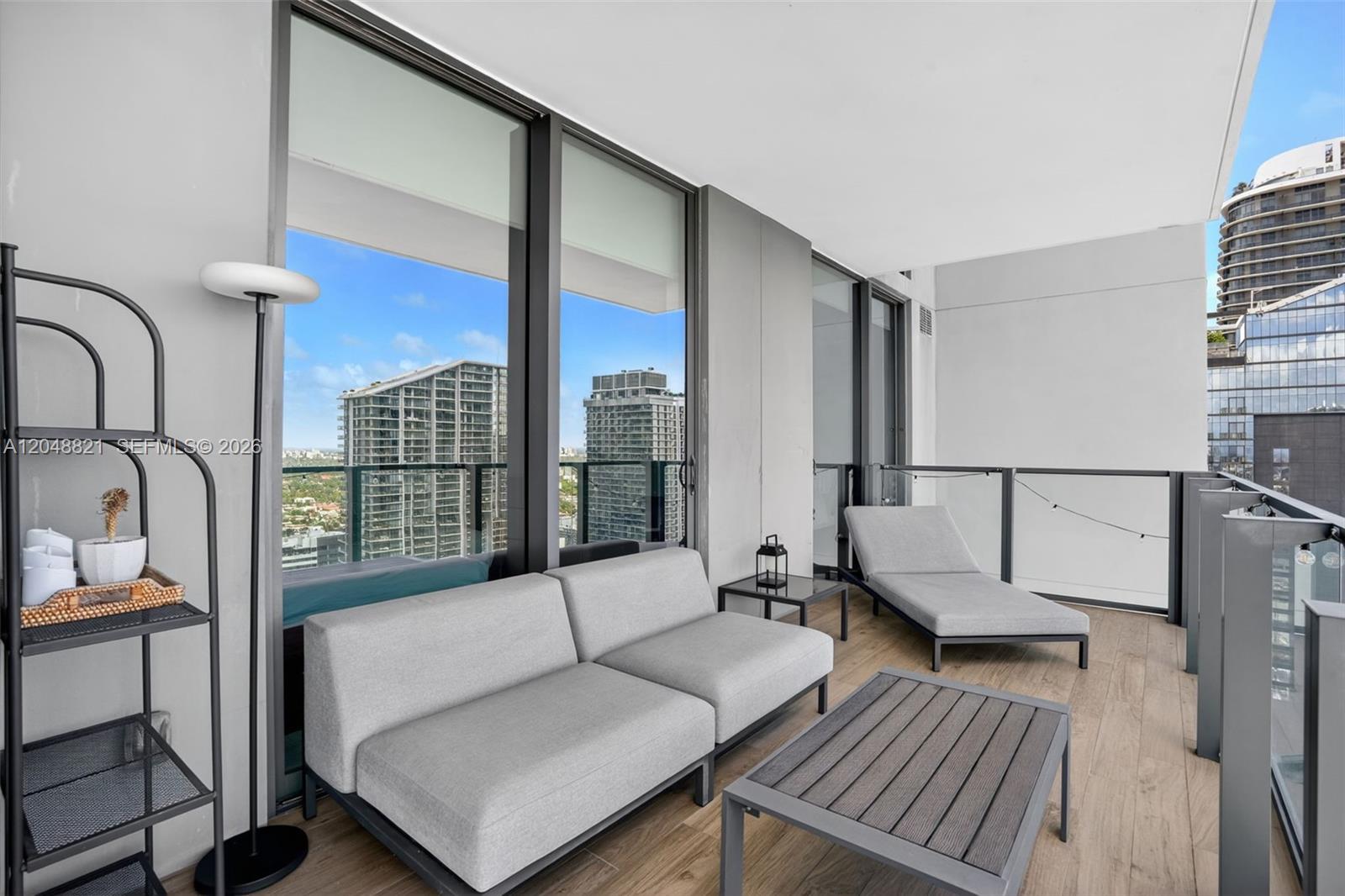 A modern balcony features gray outdoor furniture, a coffee table, and views of city buildings — 68 SE 6th St # 3710, Miami FL 33131, MIAMI, FL