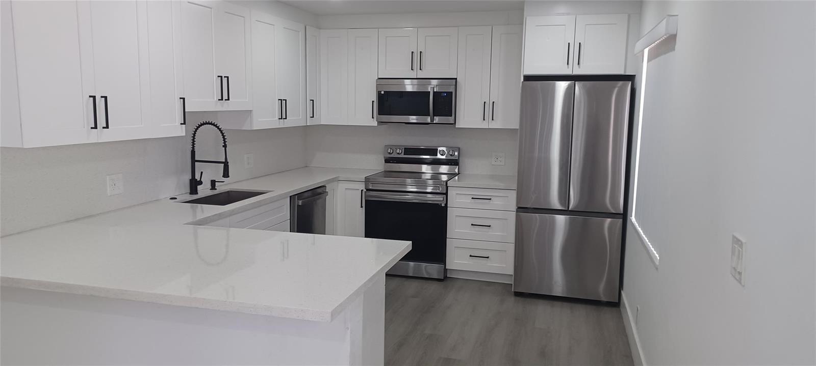 A modern kitchen features white cabinets, stainless steel appliances, and light-colored quartz countertops — 630 N 58th Avenue, Hollywood FL 33021, HOLLYWOOD, FL