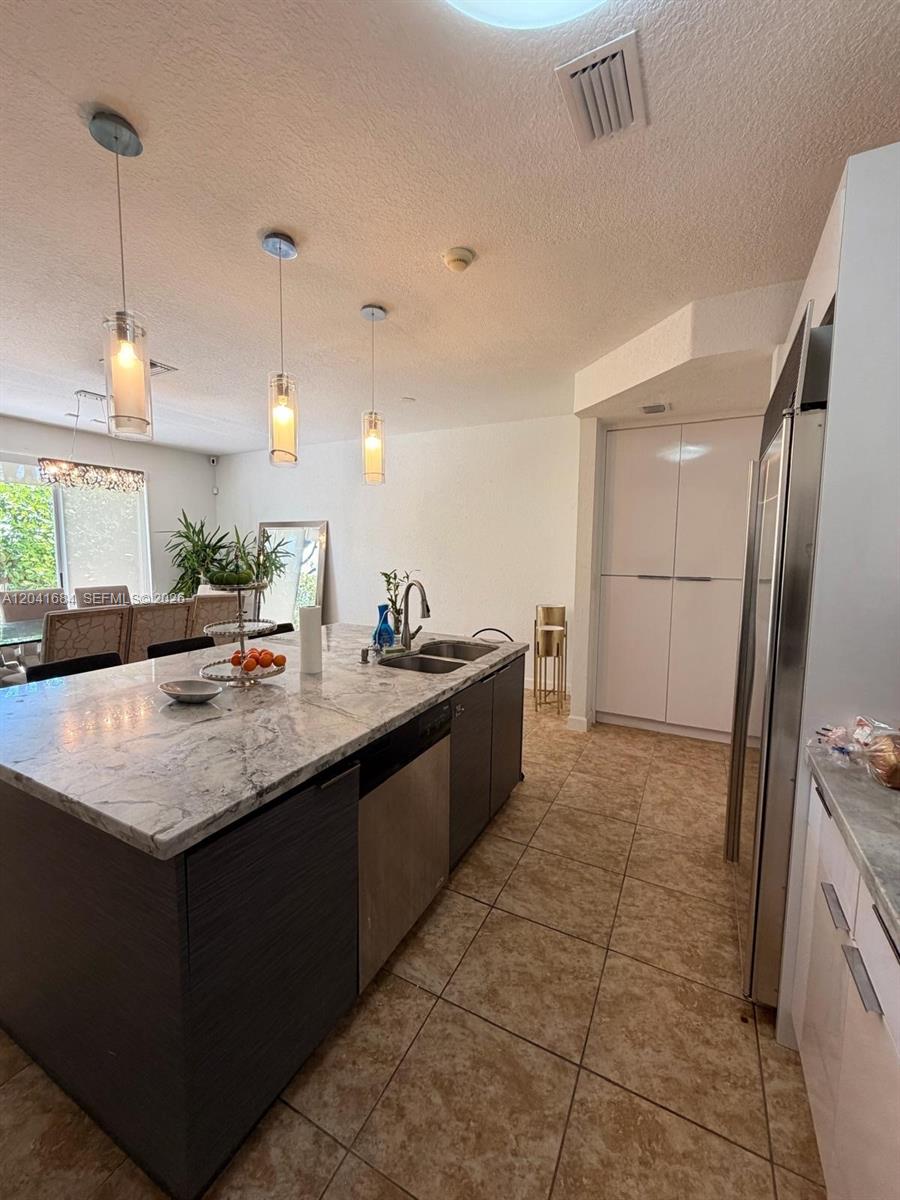 A kitchen features a marble-topped island, dark cabinetry, stainless steel appliances, and tile flooring — 10958 NW 86th Ter, Doral FL 33178, DORAL, FL