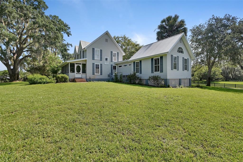 A two-story light gray house with a metal roof sits on a large grassy lawn — 900 E KICKLIGHTER ( 15+/- ACRES) ROAD, LAKE HELEN, FL