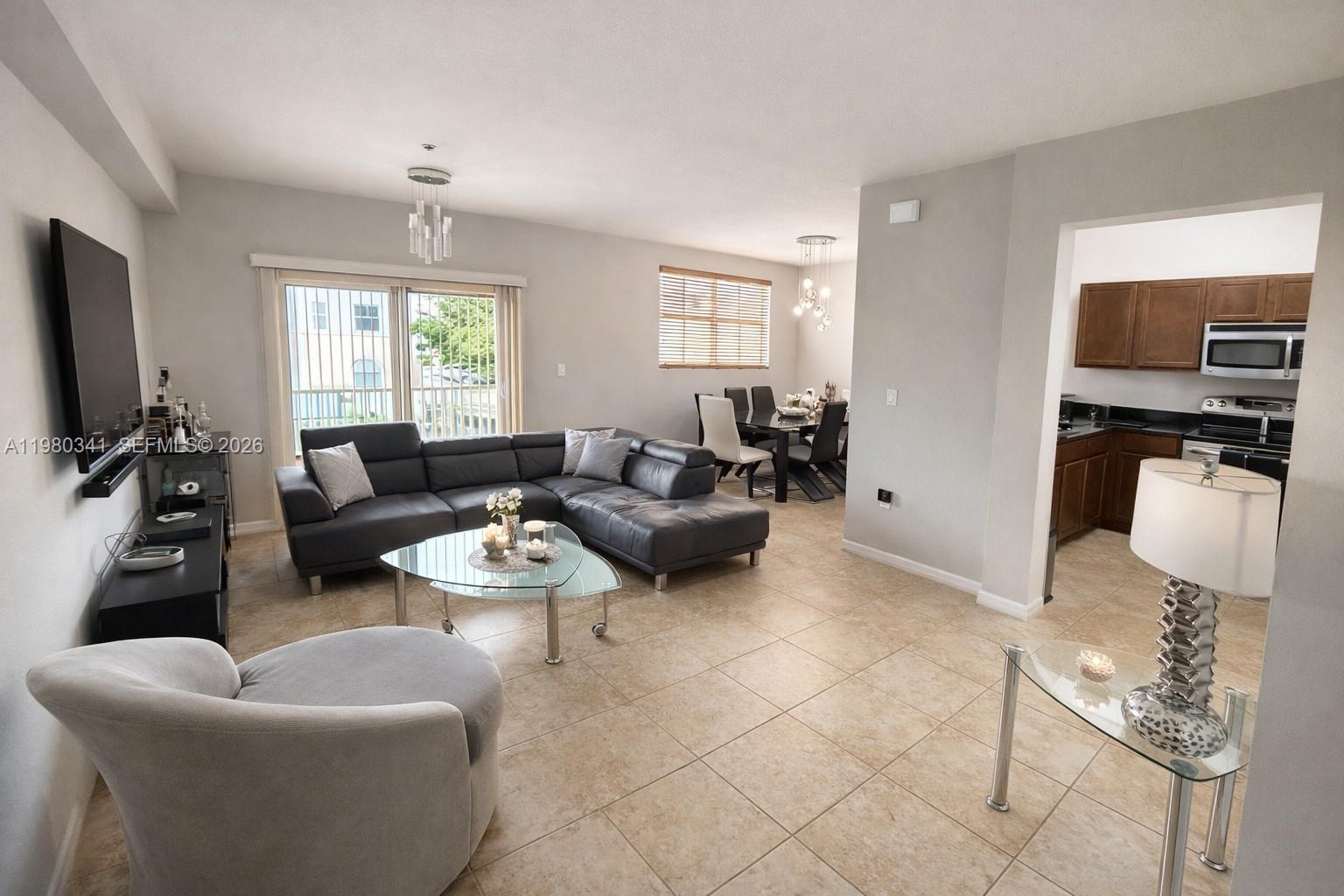 An open-concept living and dining area features tile flooring, a sectional sofa, and a kitchen — 8899 NW 107th Ct # 219, Doral FL 33178, DORAL, FL
