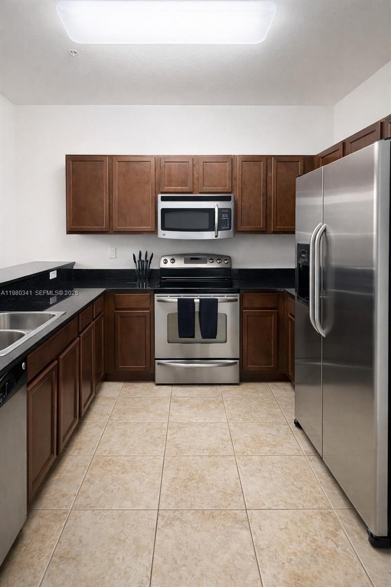 A kitchen features dark wood cabinets, stainless steel appliances, and black countertops — 8899 NW 107th Ct # 219, Doral FL 33178, DORAL, FL