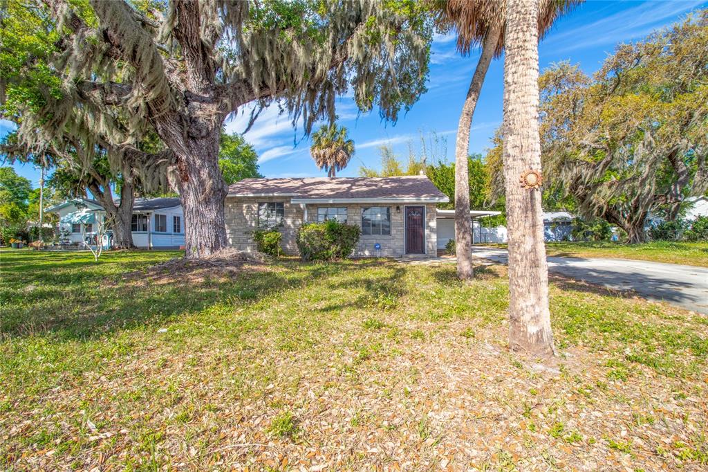 A single-story stone house sits on a grassy lot shaded by large, moss-covered oak trees — 1503 10TH AVENUE W, PALMETTO, FL