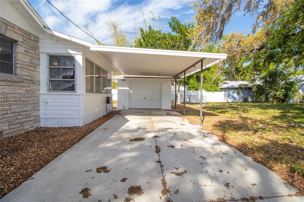A white house exterior features a concrete driveway leading to a detached garage with a carport — 1503 10TH AVENUE W, PALMETTO, FL