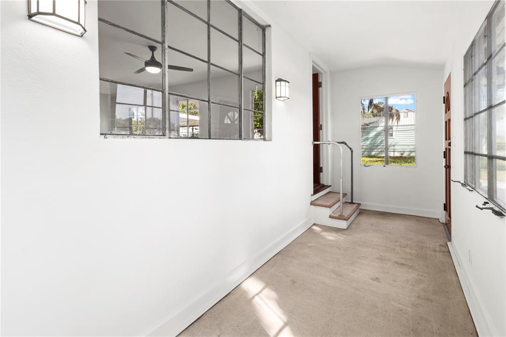 A bright, white-walled enclosed porch features a concrete floor, grid-style windows, and small steps — 1503 10TH AVENUE W, PALMETTO, FL