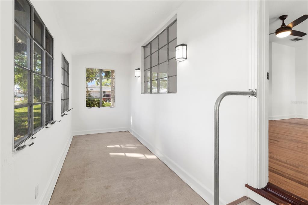 A sunroom with white walls, multiple grid-pane windows, and a metal handrail near the entrance — 1503 10TH AVENUE W, PALMETTO, FL