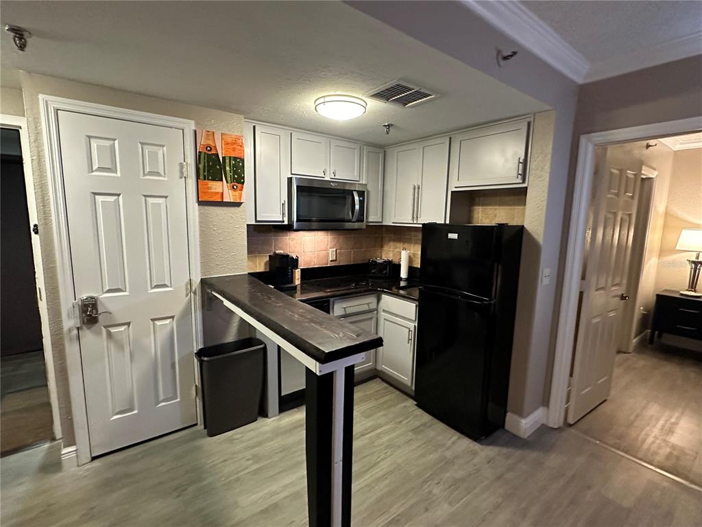 A kitchen features white cabinets, black appliances, a dark wood breakfast bar, and light flooring — 6165 CARRIER DRIVE UNIT 1203, ORLANDO, FL