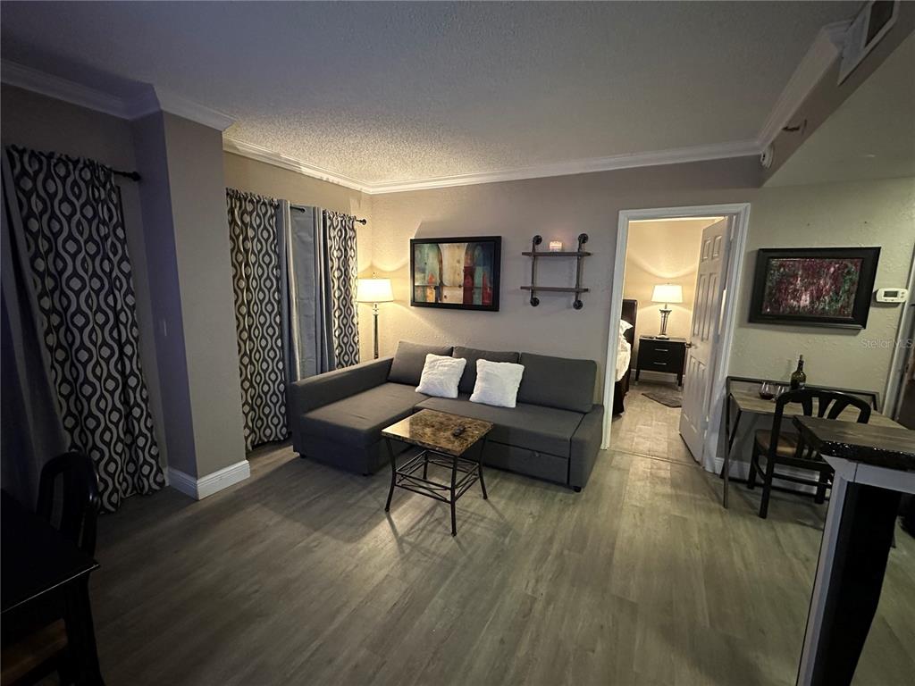A living room features a gray sectional sofa, a small coffee table, and wood-look flooring — 6165 CARRIER DRIVE UNIT 1203, ORLANDO, FL