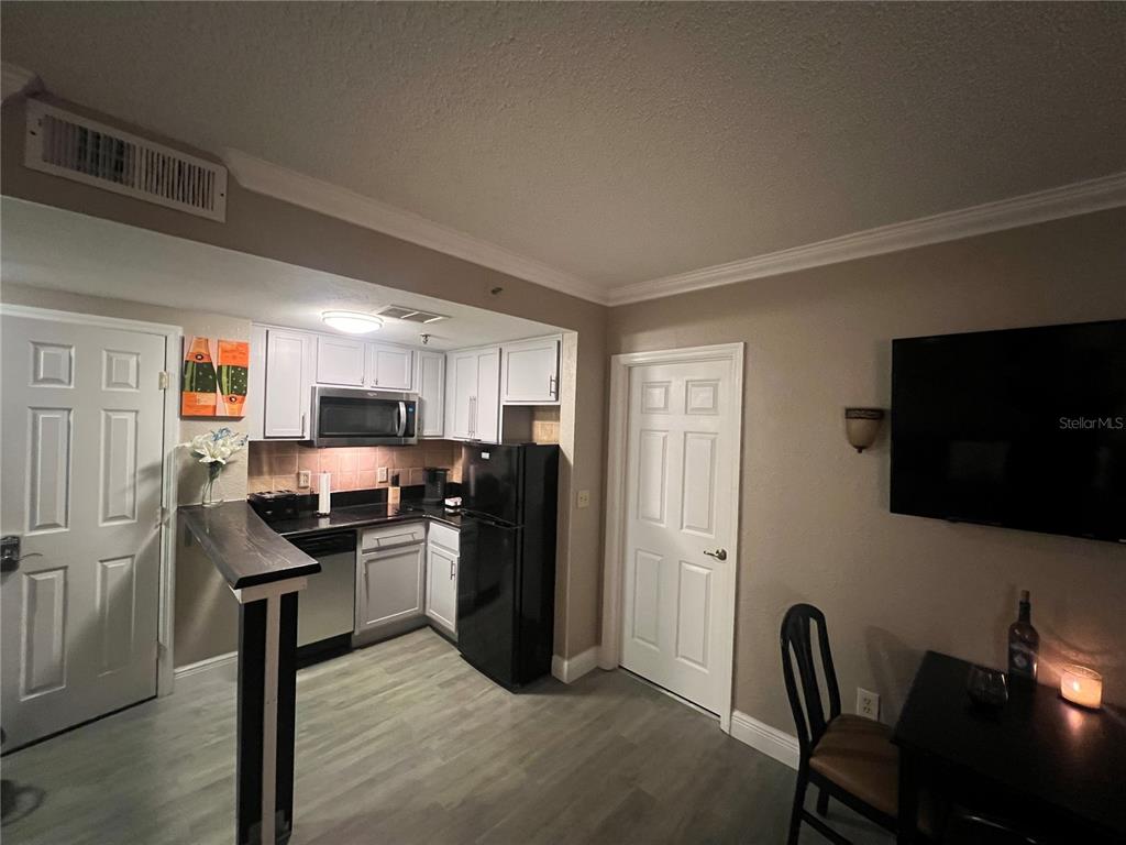 A kitchen with white cabinets, black appliances, and a breakfast bar opens to a room — 6165 CARRIER DRIVE UNIT 1203, ORLANDO, FL