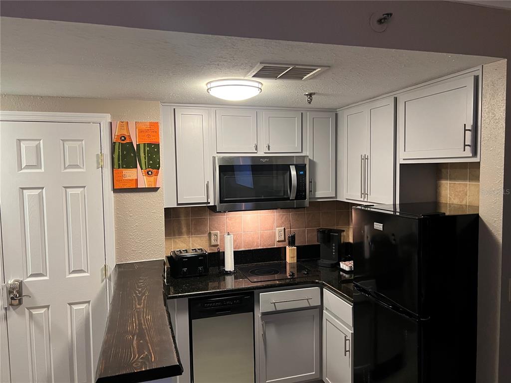 A kitchen features light gray cabinets, black appliances, dark countertops, and a wooden breakfast bar — 6165 CARRIER DRIVE UNIT 1203, ORLANDO, FL