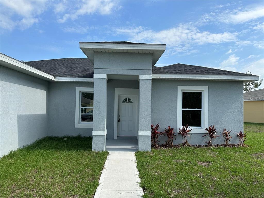 The exterior of a gray stucco house features a covered entryway and a concrete walkway — 149 MAPLE DRIVE, POINCIANA, FL