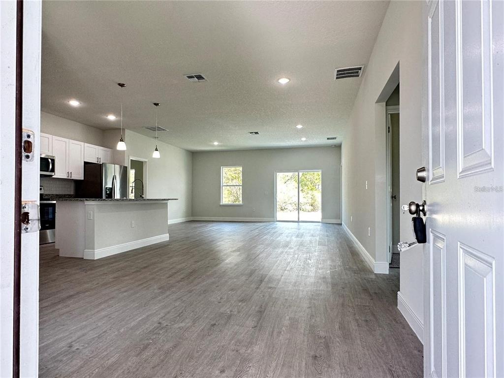 An open-concept living area features light wood-look flooring, a kitchen island, and sliding glass doors — 149 MAPLE DRIVE, POINCIANA, FL