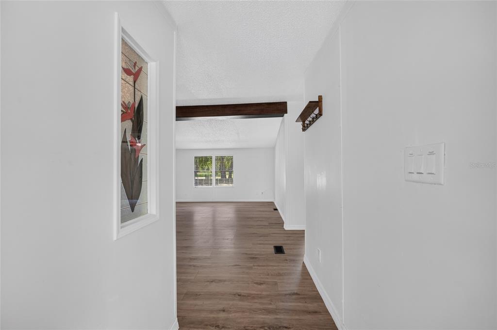 A hallway with wood-look flooring leads to a living area featuring a dark ceiling beam — 3353 SW 181ST COURT, DUNNELLON, FL