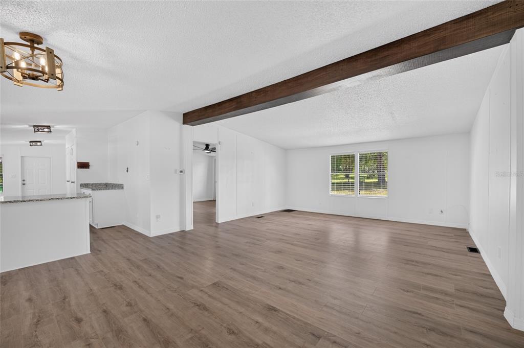 An open-concept living area features white walls, wood-look flooring, and a prominent dark wood beam — 3353 SW 181ST COURT, DUNNELLON, FL