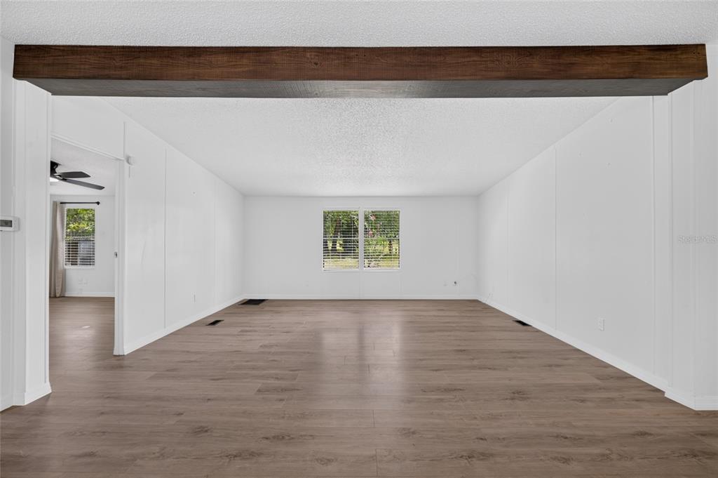 A spacious, empty living room features white walls, wood-look flooring, and a dark wood ceiling beam — 3353 SW 181ST COURT, DUNNELLON, FL