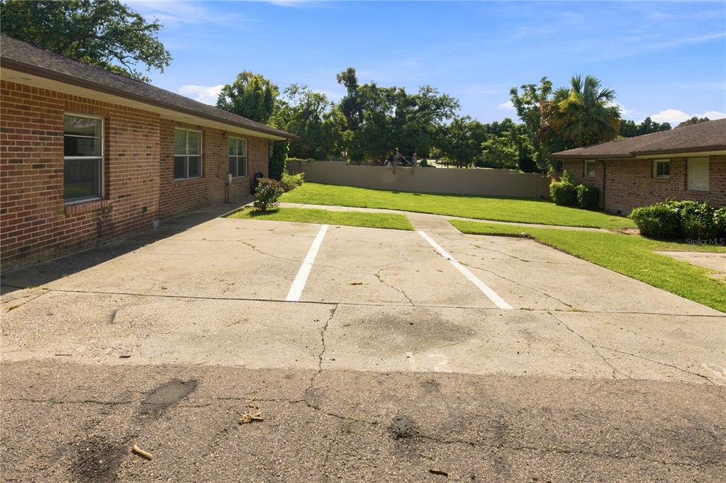A concrete parking area sits between two brick buildings with a grassy lawn behind — 101 LAKE HUNTER DRIVE UNIT 12, LAKELAND, FL