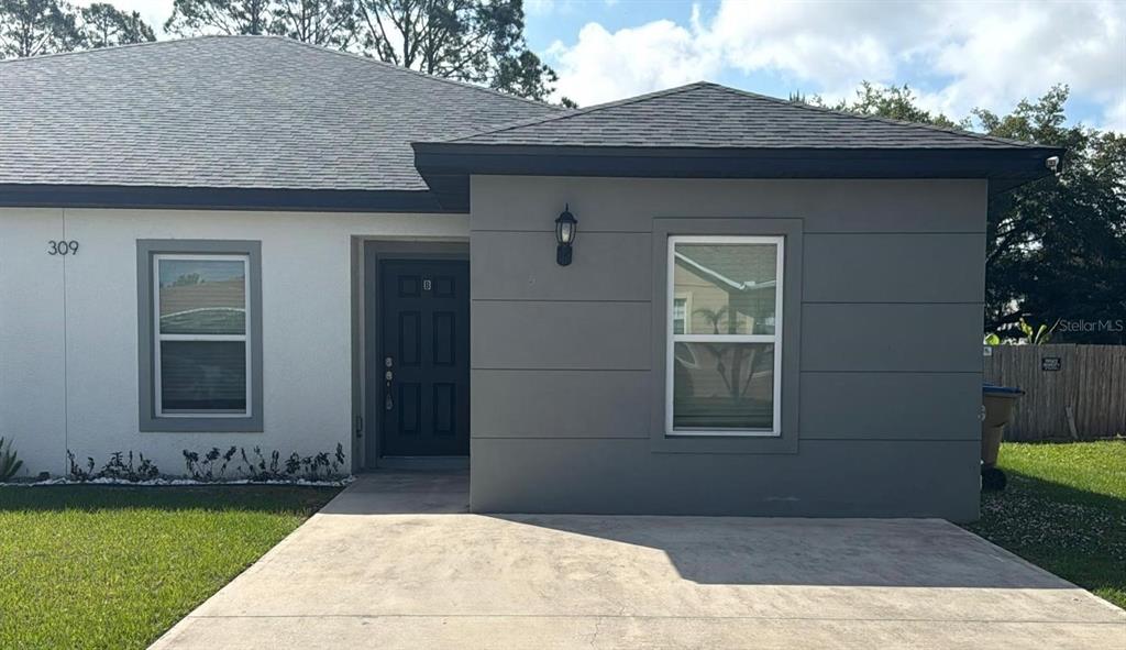 A single-story house exterior features a gray facade, a dark front door, and a concrete driveway — 309 CLERMONT DRIVE UNIT B, POINCIANA, FL