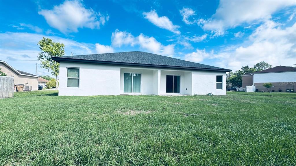 The back exterior of a white, single-story house with a lawn and sliding glass doors — 309 CLERMONT DRIVE UNIT B, POINCIANA, FL