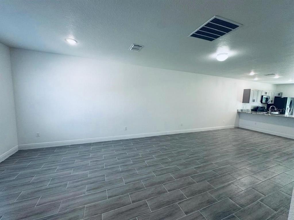 A spacious room with gray wood-look tile flooring and a kitchen in the background — 309 CLERMONT DRIVE UNIT B, POINCIANA, FL