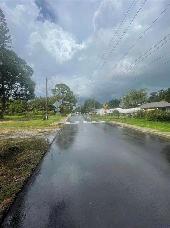 A wet asphalt road leads toward a crosswalk in a residential neighborhood under a cloudy sky — 0 ORANGE GROVE S, NOKOMIS, FL