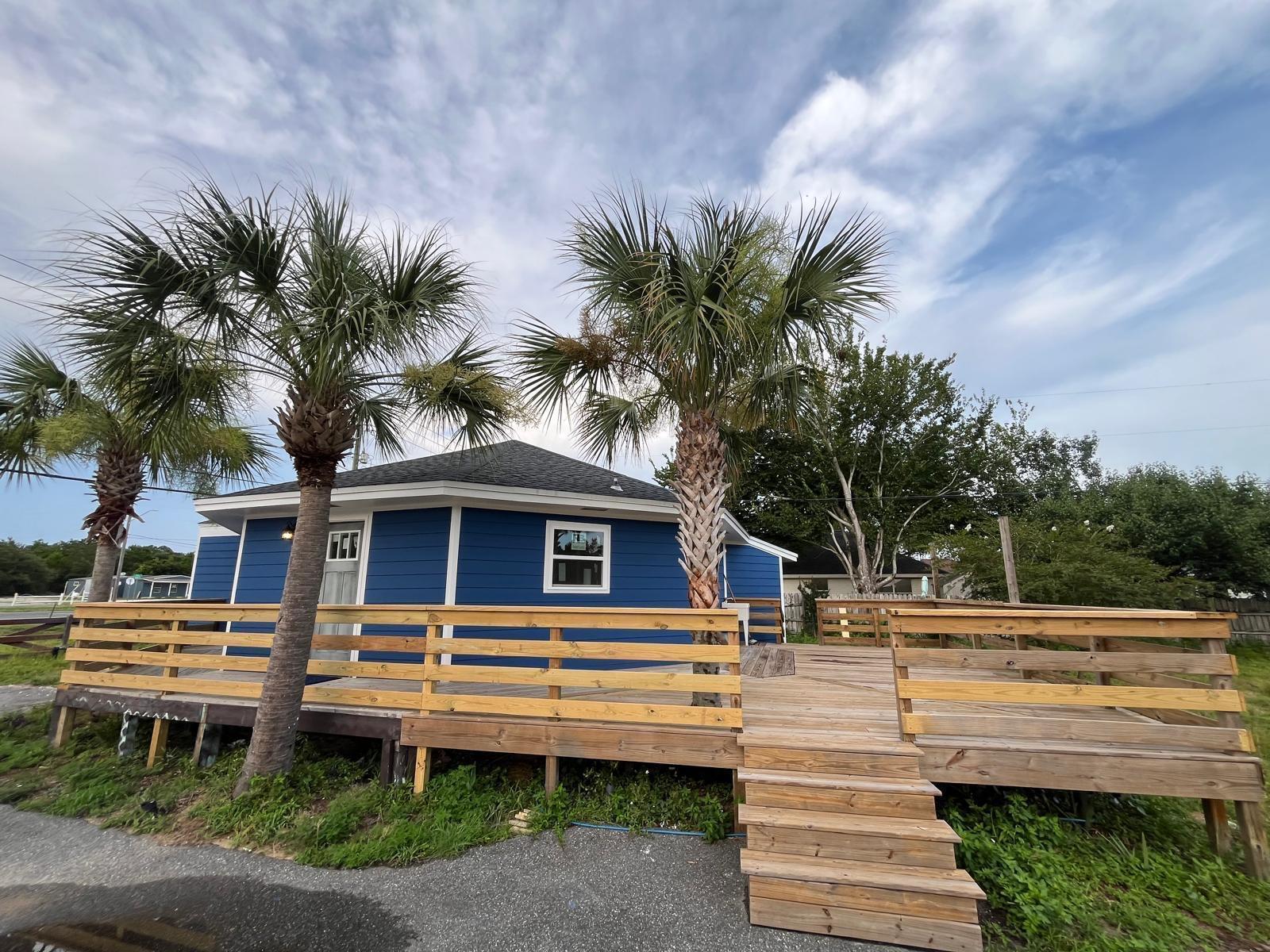 A blue house with a wooden deck and stairs sits behind two palm trees — 2040 Falconhurst Place # 2040, FL 32566, FL